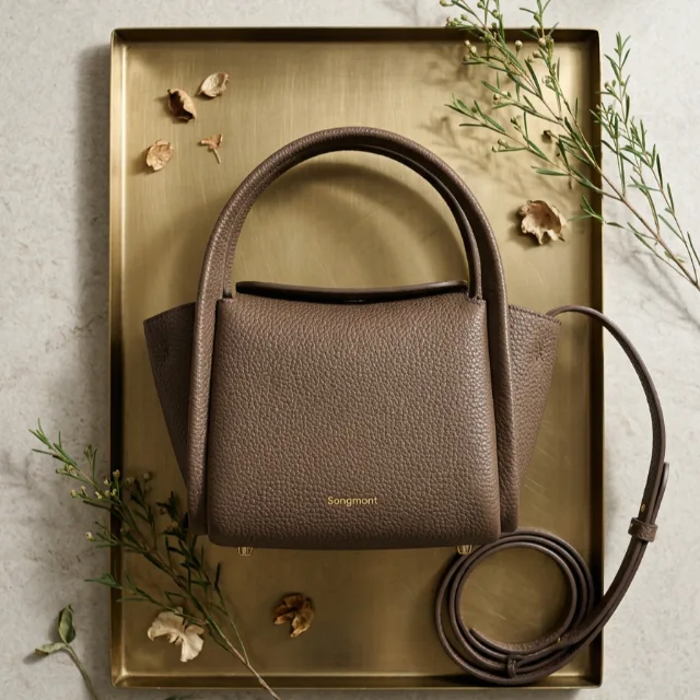 The handbag styled flat on a brass tray with foliage